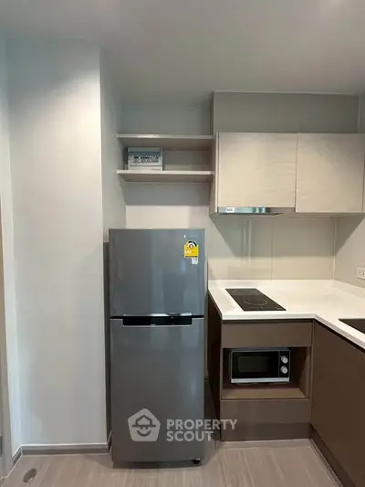 Modern kitchen with sleek appliances and minimalist design, featuring a fridge and built-in microwave.