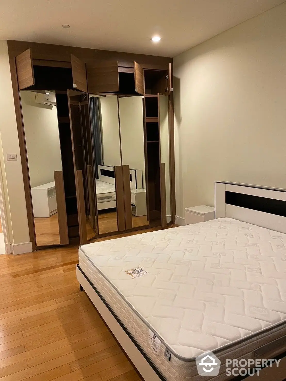 Spacious bedroom with polished hardwood floors and built-in mirrored wardrobe, offering a sleek and modern living space.