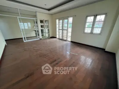 Spacious empty room with wooden flooring and large windows for natural light.