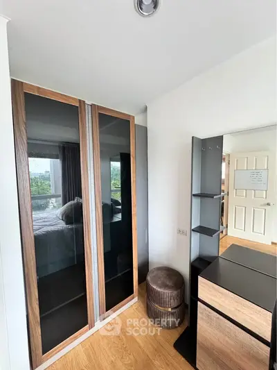 Modern bedroom with sleek wardrobe and stylish dresser, featuring a cozy stool and natural light.