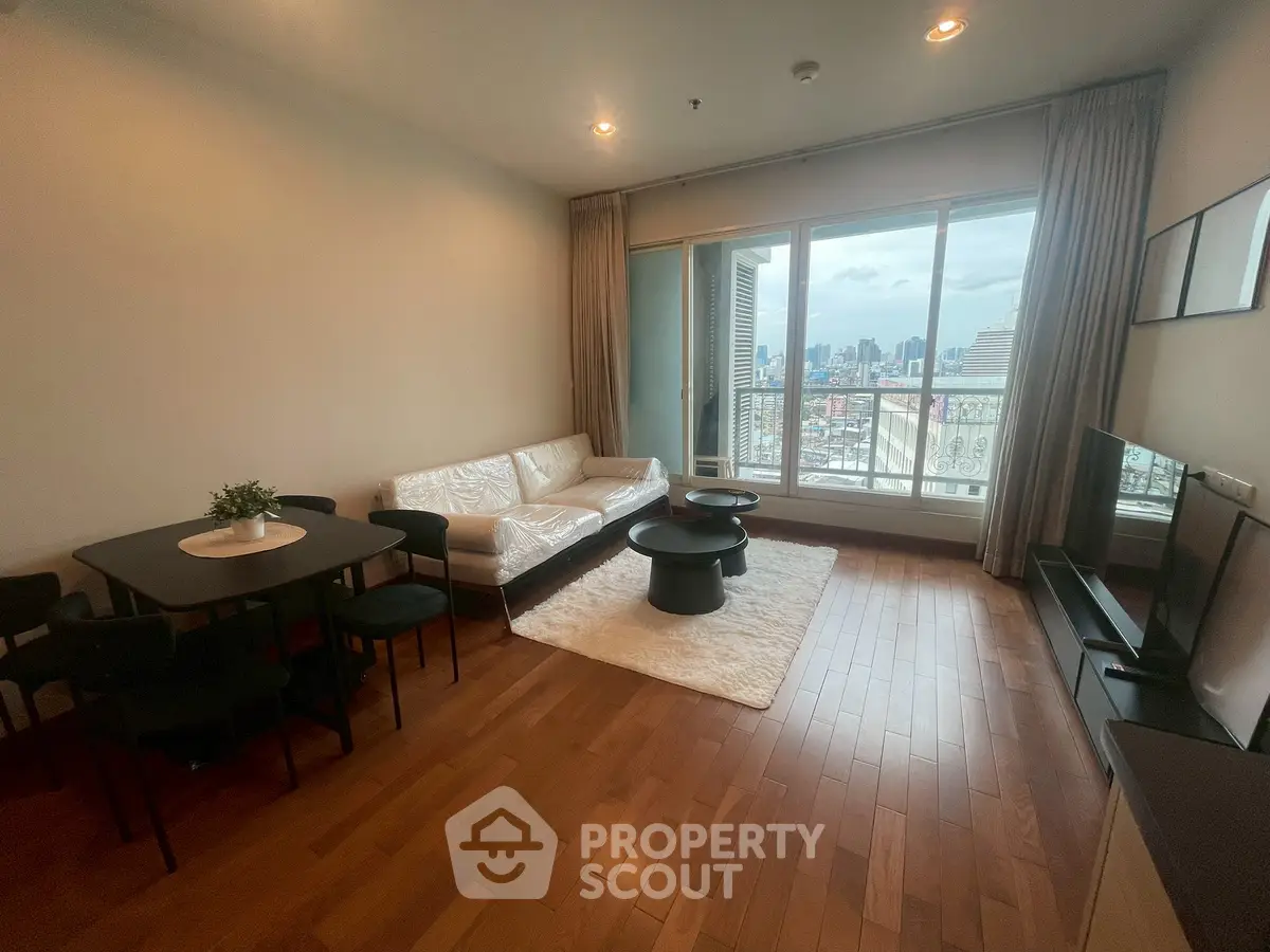 Spacious living room with city view, wooden flooring, and modern furniture in a high-rise apartment.