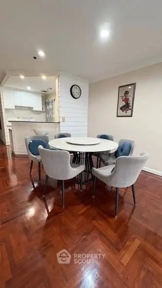 Elegant dining area with round table and plush chairs, adjacent to modern kitchen.