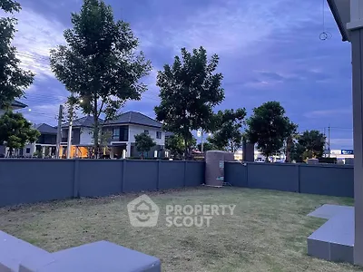 Spacious backyard with lush lawn and modern fence in suburban neighborhood at dusk.