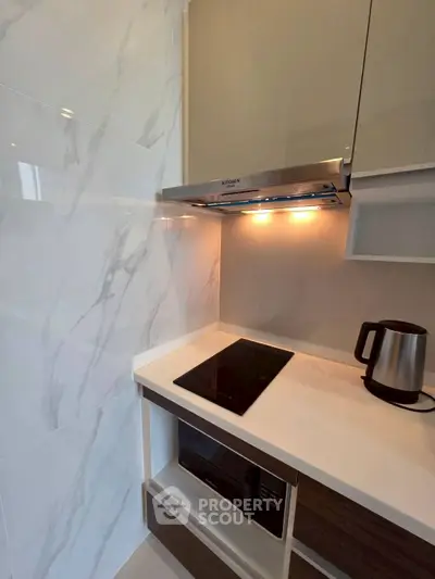 Modern kitchen with sleek cooktop and kettle, featuring elegant marble backsplash and under-cabinet lighting.
