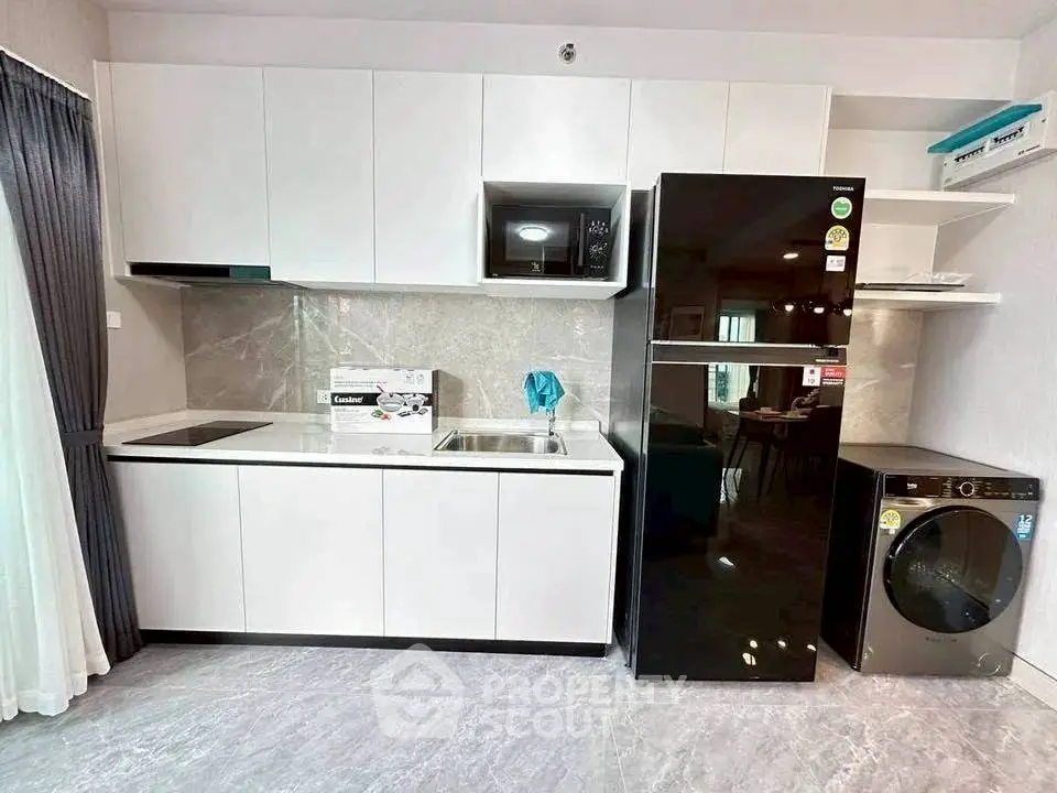 Modern kitchen with sleek white cabinets, black fridge, and washing machine in stylish apartment.