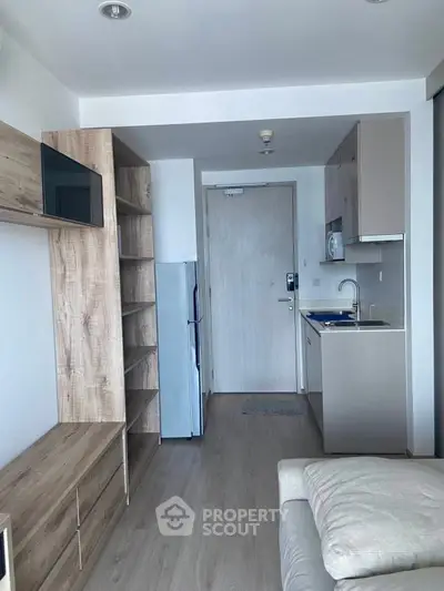 Modern studio apartment with compact kitchen and cozy living area, featuring sleek wooden cabinetry and light flooring.
