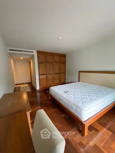 Spacious bedroom with wooden flooring and built-in wardrobe in modern apartment.