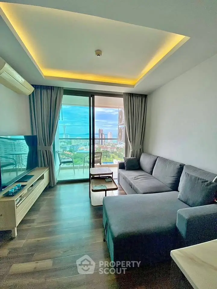 Modern living room with large windows and stunning city view, featuring a cozy gray sofa and sleek TV unit.