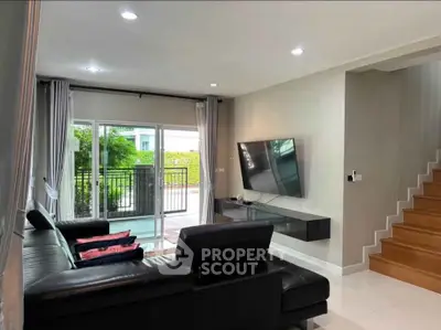 Modern living room with sleek black sofa, wall-mounted TV, and view of outdoor greenery.