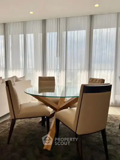 Elegant dining area with glass table and plush chairs in a modern apartment with floor-to-ceiling windows.