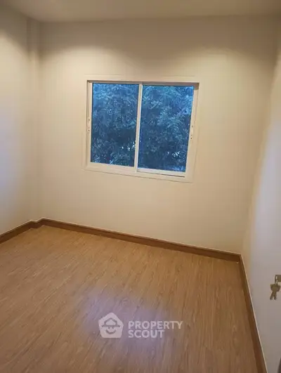 Cozy unfurnished room with wooden flooring and a window view of lush greenery.