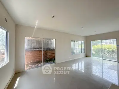 Spacious unfurnished living room with large windows and sliding glass doors opening to a garden view.