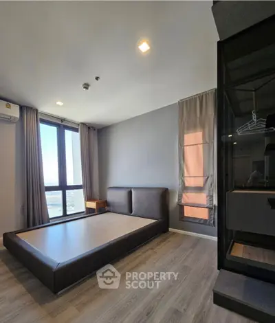 Modern bedroom with large window and minimalist design in high-rise apartment.