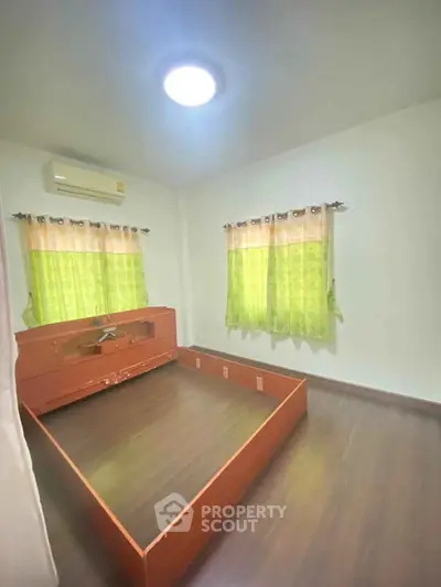 Spacious bedroom with wooden flooring and natural light, featuring air conditioning and stylish green curtains.