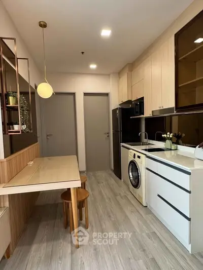 Modern kitchen with washing machine and sleek dining area in compact apartment.
