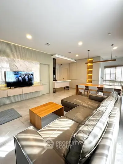 Modern living room with sleek furniture and open layout, featuring a large TV and dining area.