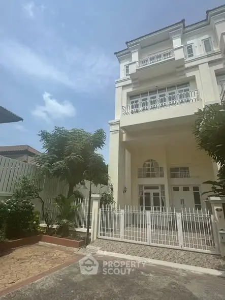 Elegant multi-story building with gated entrance and lush greenery under a clear blue sky.