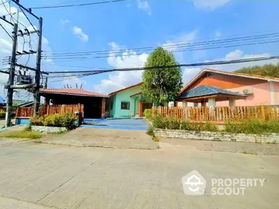 Charming single-story home with terracotta roof tiles and a spacious front yard, featuring a cozy porch and a vibrant wooden fence, set against a clear blue sky.