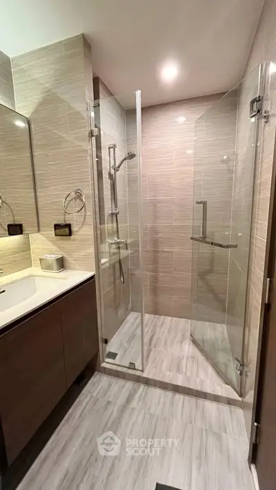 Modern bathroom with glass shower enclosure and sleek vanity in upscale apartment.