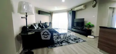 Modern living room with sleek black leather sofa, large TV, and stylish decor in a bright, airy apartment.