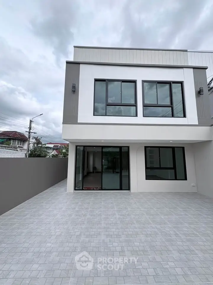 Modern two-story house with large windows and spacious tiled driveway, perfect for family living.