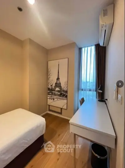 Cozy bedroom with wooden flooring, desk, and Eiffel Tower artwork, perfect for a serene retreat.