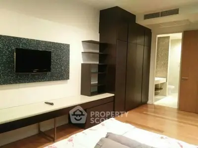 Modern bedroom with sleek furniture and wall-mounted TV, featuring a view into a stylish bathroom.