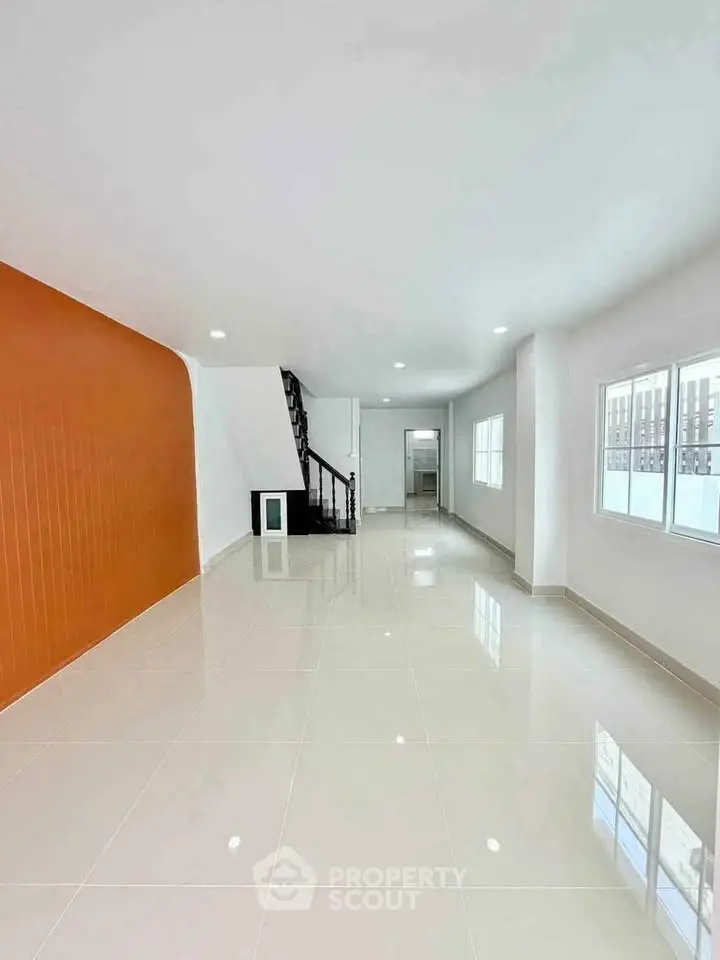 Spacious modern living room with glossy tiled floors and vibrant orange accent wall.