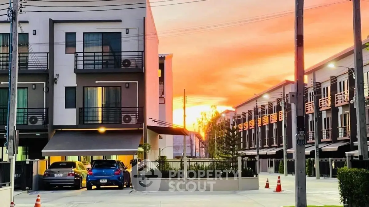 Modern townhouse complex at sunset with parked cars and vibrant sky.