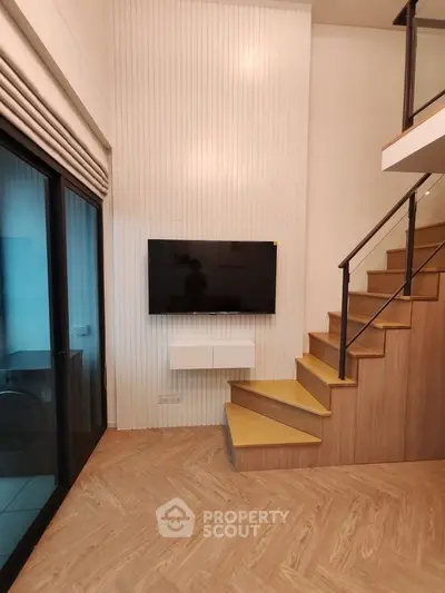 Modern living room with stylish staircase and wall-mounted TV, featuring elegant wood flooring and large window.