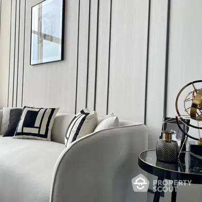 Elegant living room corner with plush white sofa, chic cushions, and a modern side table, accented by sophisticated wall paneling and art.