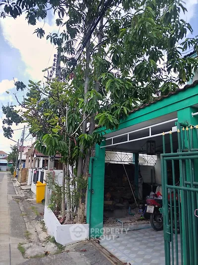 Charming residential street view with vibrant green house and lush trees, perfect for serene living.