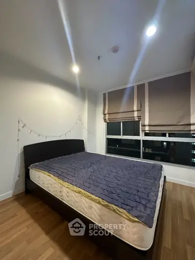 Cozy bedroom with large windows offering a city view, complemented by warm lighting and minimalist decor, perfect for urban living.