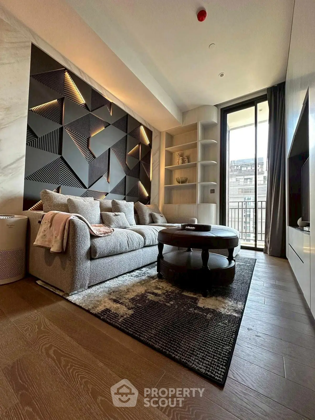 Modern living room with stylish geometric wall design and cozy seating area, leading to a balcony with city views.