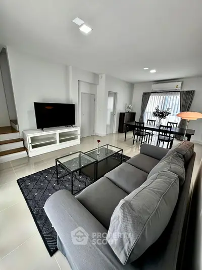 Modern living room with sleek furniture and open layout, featuring a cozy gray sofa and large TV.