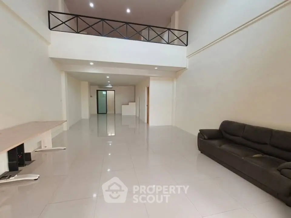 Spacious modern living room with high ceiling and mezzanine, featuring sleek tile flooring and contemporary furniture.