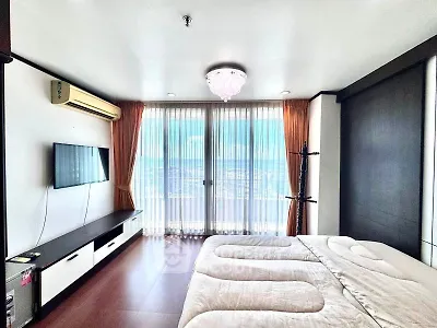 Modern bedroom with large windows and city view, featuring a wall-mounted TV and elegant lighting.