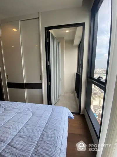 Modern bedroom with balcony and city view, featuring sleek wardrobe and cozy bedding.