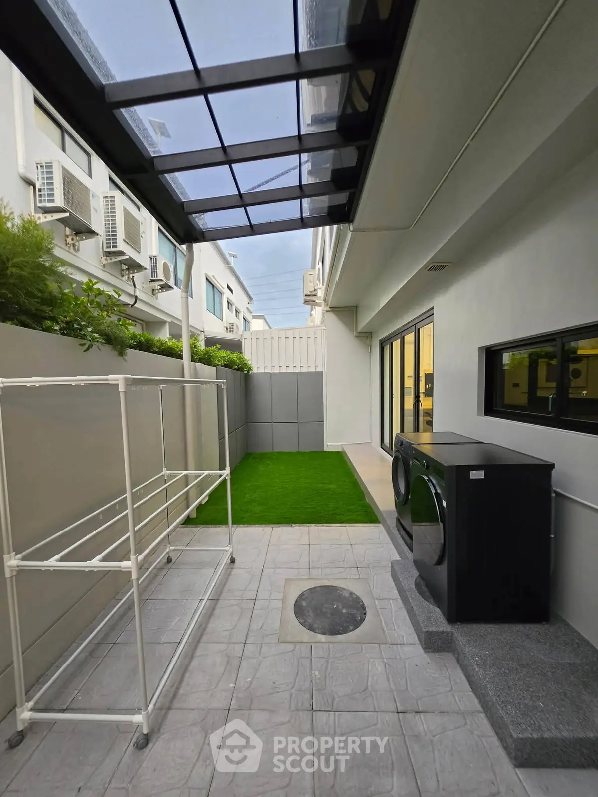 Modern outdoor laundry area with washing machine and drying rack in sleek residential setting.