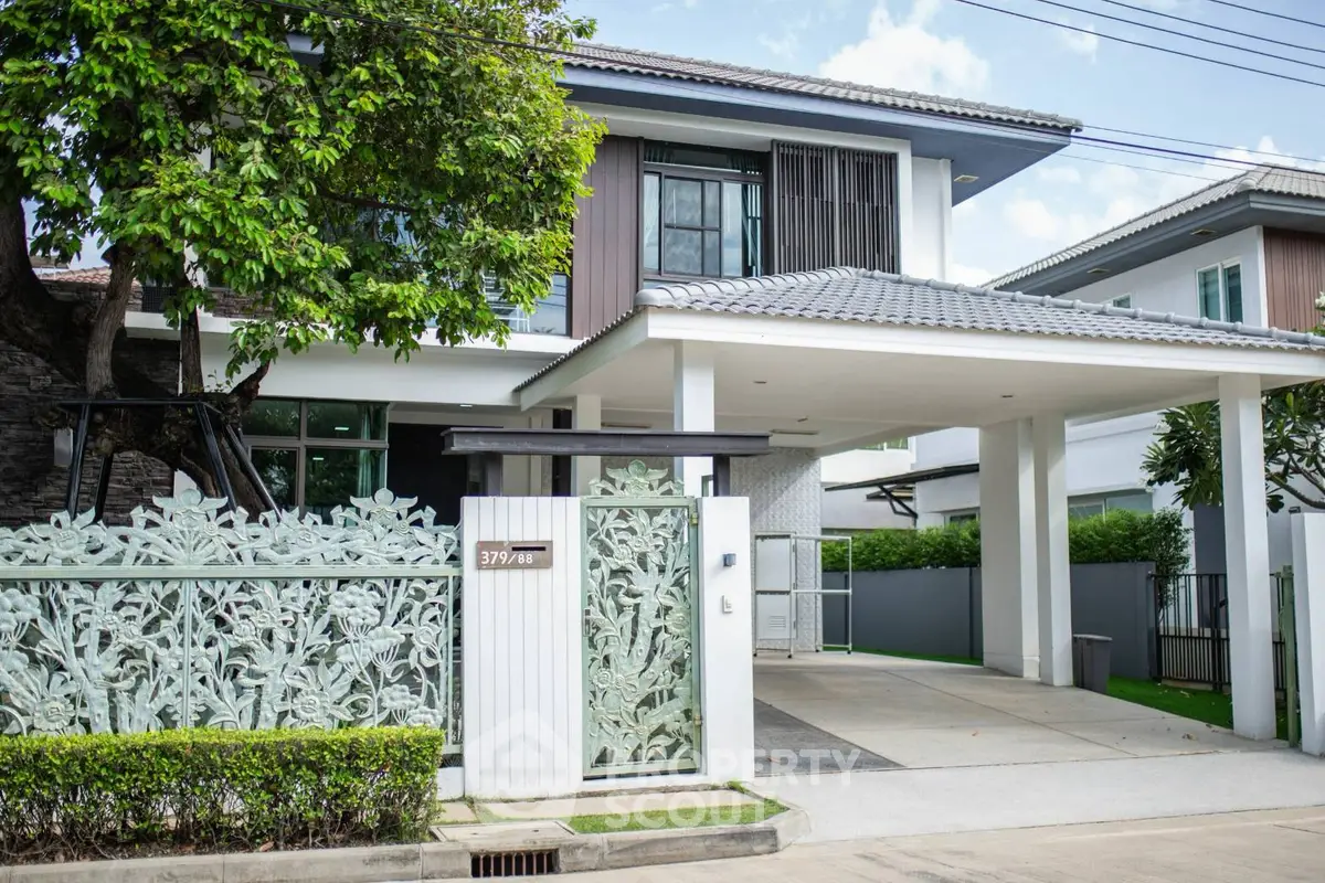 Modern two-story house with stylish gate and lush greenery in a serene neighborhood.