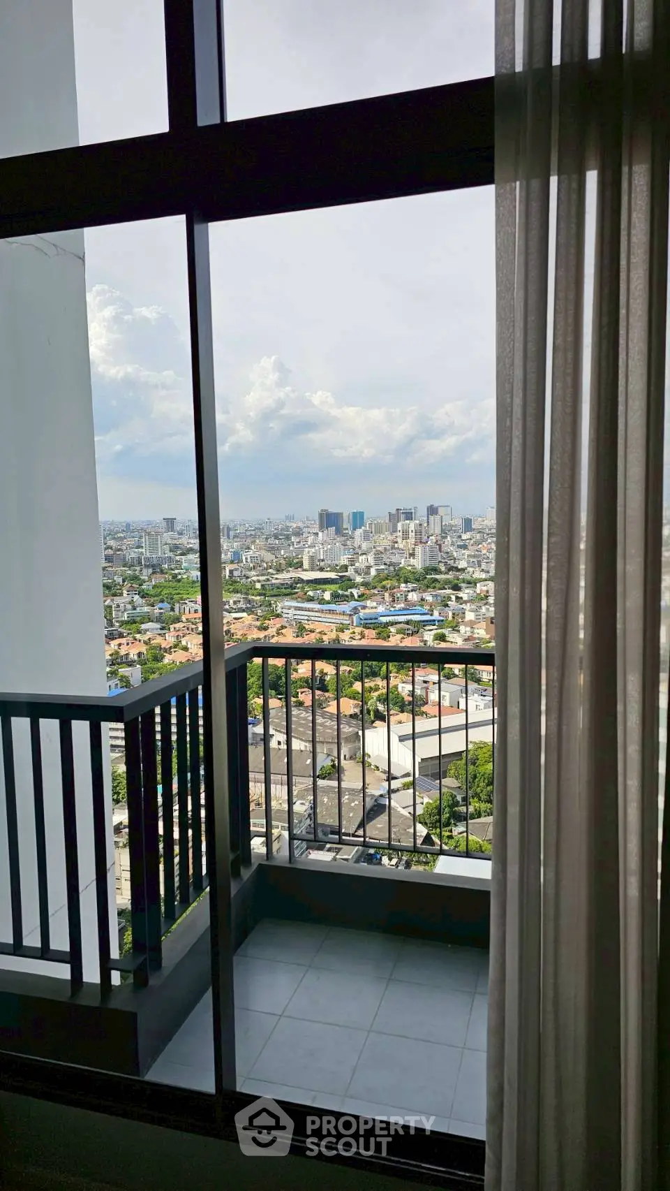Stunning cityscape view from a high-rise balcony with glass railing and curtains.