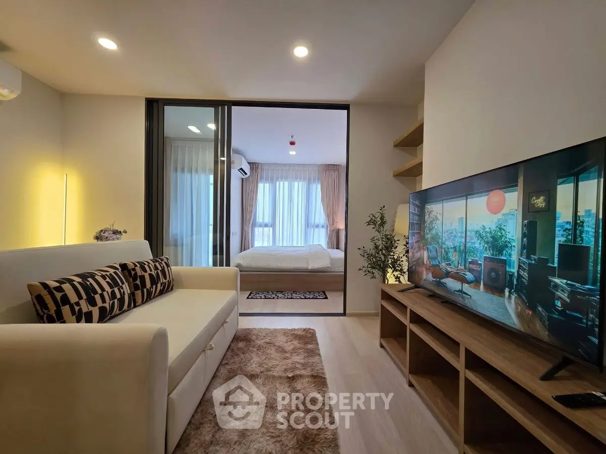 Modern living room with cozy sofa and large TV, open view to bedroom