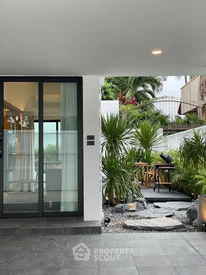 Modern home with glass doors opening to a lush garden and outdoor seating area.