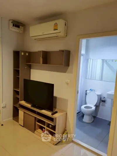 Compact living room with TV and air conditioning next to a bathroom in a modern apartment.
