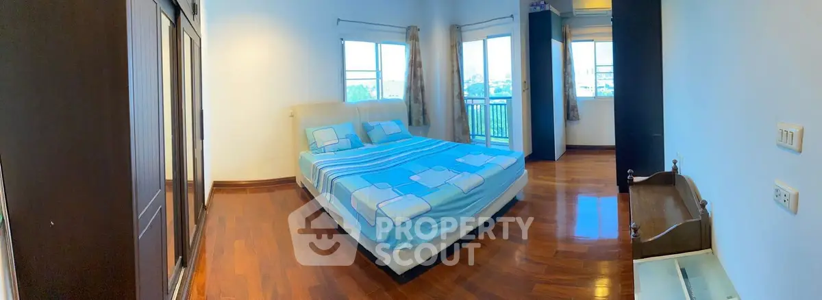 Spacious bedroom with wooden flooring and large windows offering natural light and views.