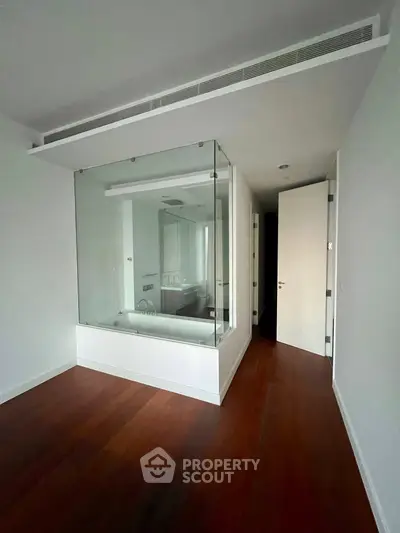 Modern interior with glass-enclosed bathtub and wooden flooring, showcasing sleek design and luxury features.