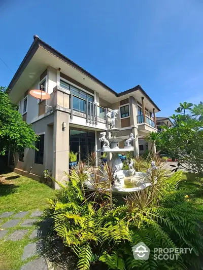 Stunning two-story house with lush garden and elegant fountain under clear blue sky.