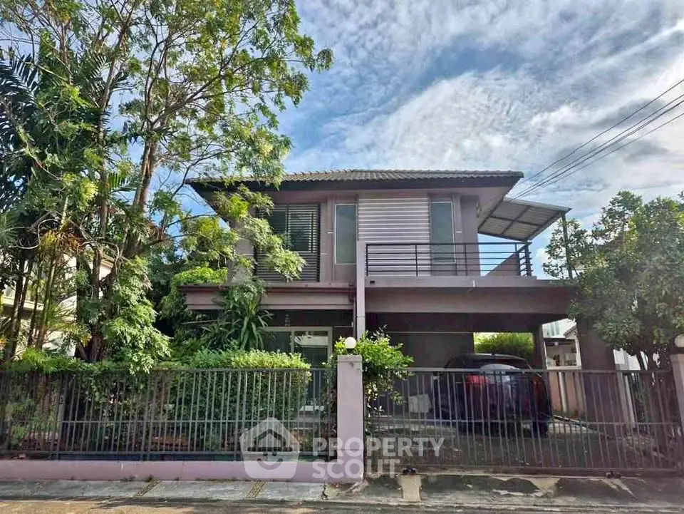 Charming two-story house with lush greenery and spacious carport in a serene neighborhood.
