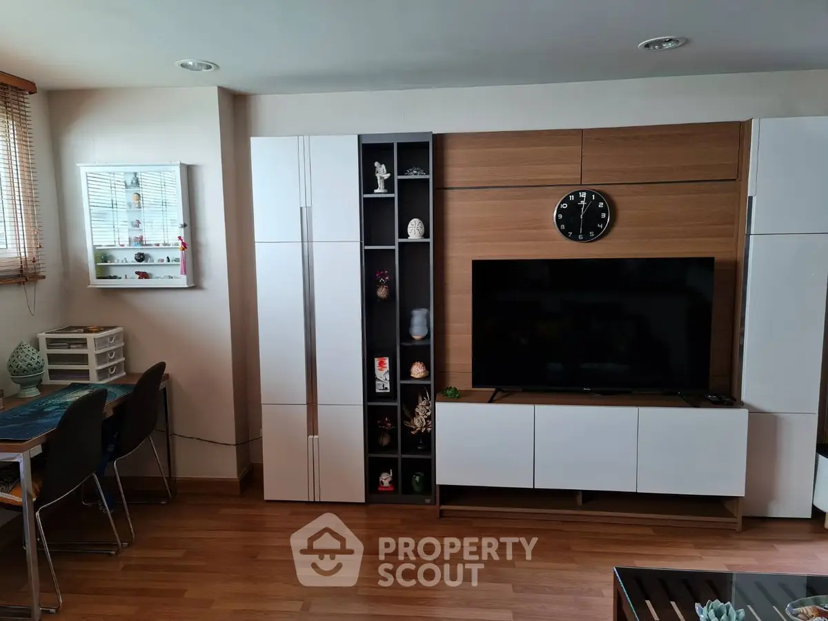Modern living room with sleek white cabinets and wall-mounted TV, featuring wooden flooring and stylish decor.