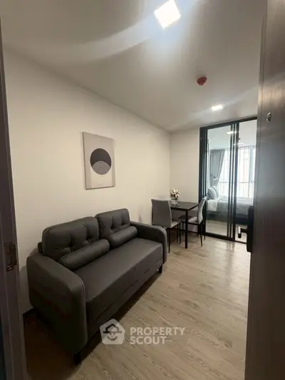 Modern apartment entrance with sleek sofa and dining area leading to a bright bedroom.